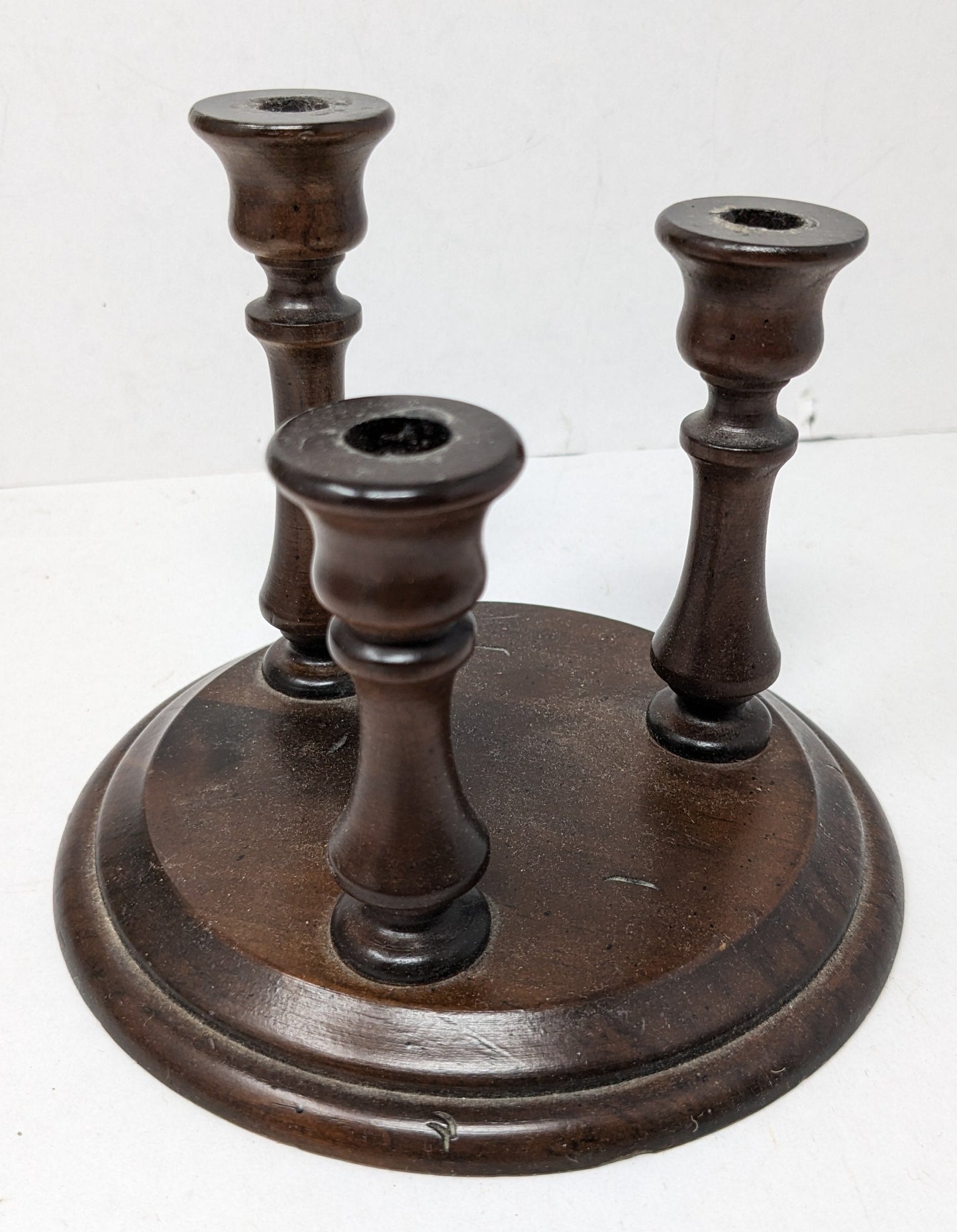 Dark wood candle holder with circular base and three candle stick slots of varying heights