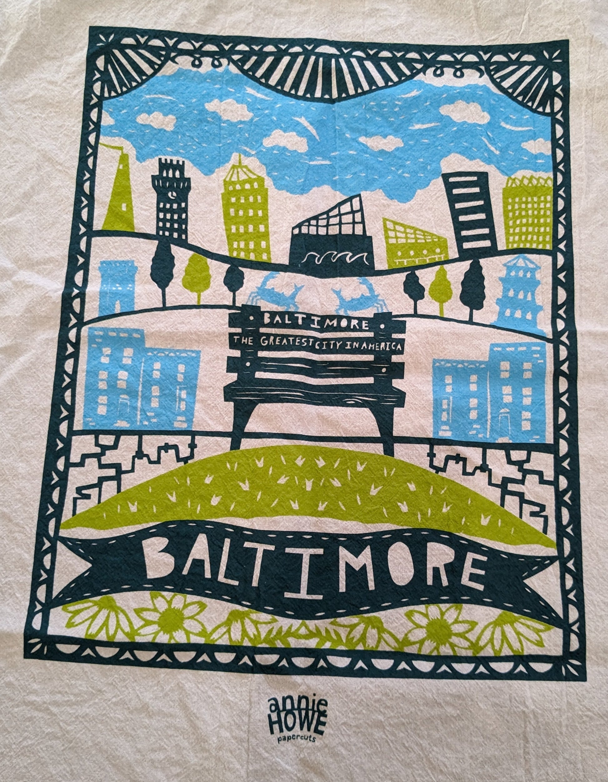 White tea towel with aqua, green, and navy papercut images of Baltimore landmarks