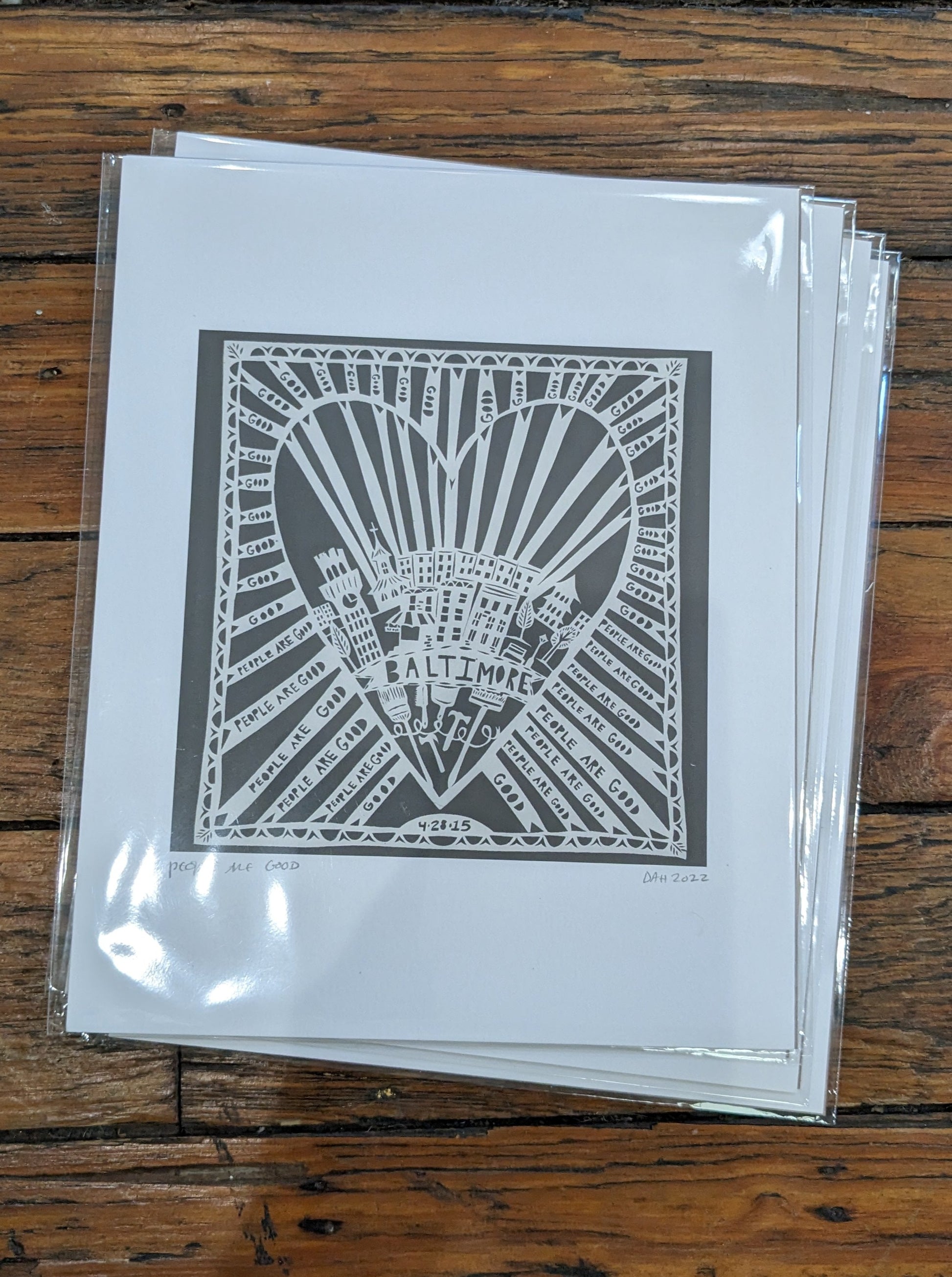 White papercut print on gray background depicting Baltimore within a heart: "People are good"