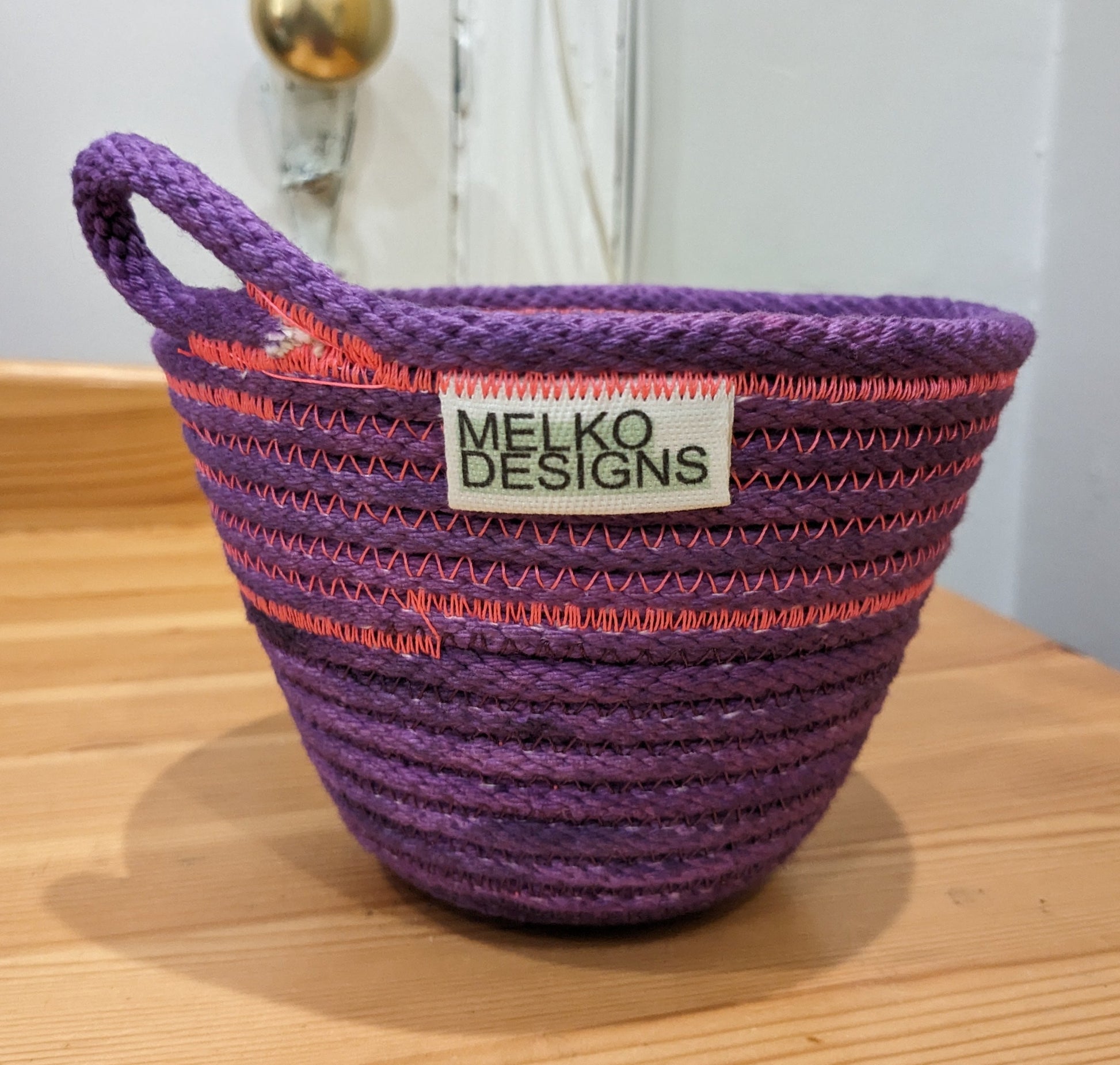 Purple rope basket with pink threading and a loop handle