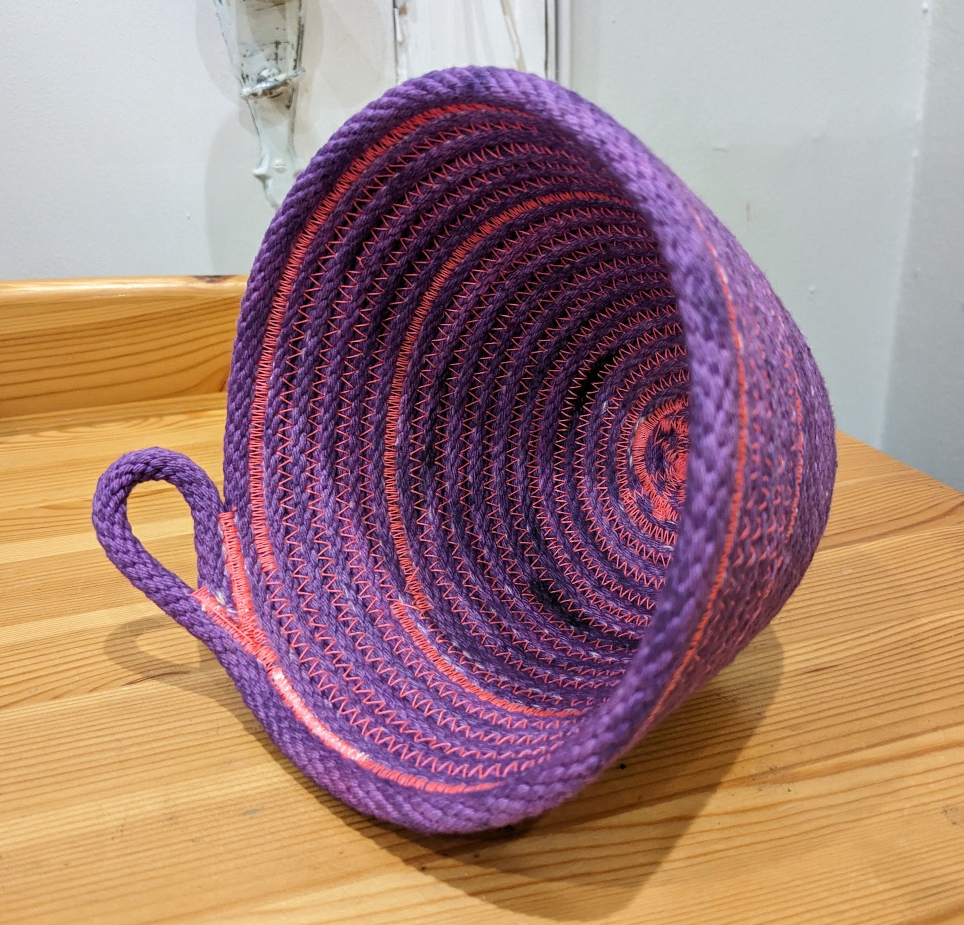 Purple rope basket with pink threading and a loop handle
