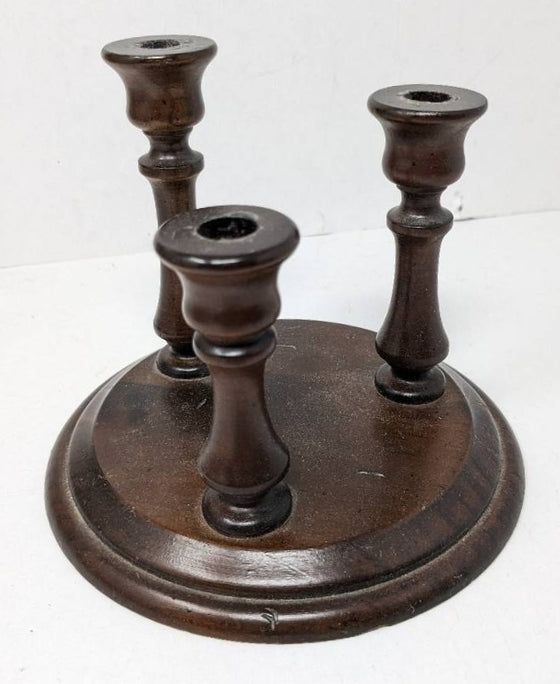 Dark wood candle holder with circular base and three candle stick slots of varying heights