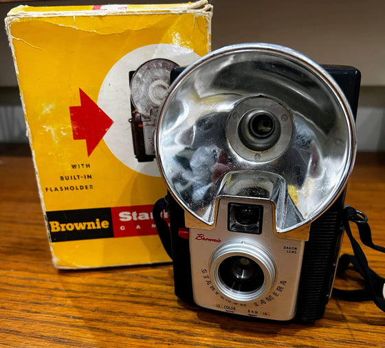 Brownie Starflash film camera with carrying strap next to original cardboard box packaging