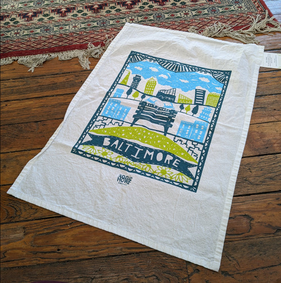 White tea towel with aqua, green, and navy papercut images of Baltimore landmarks